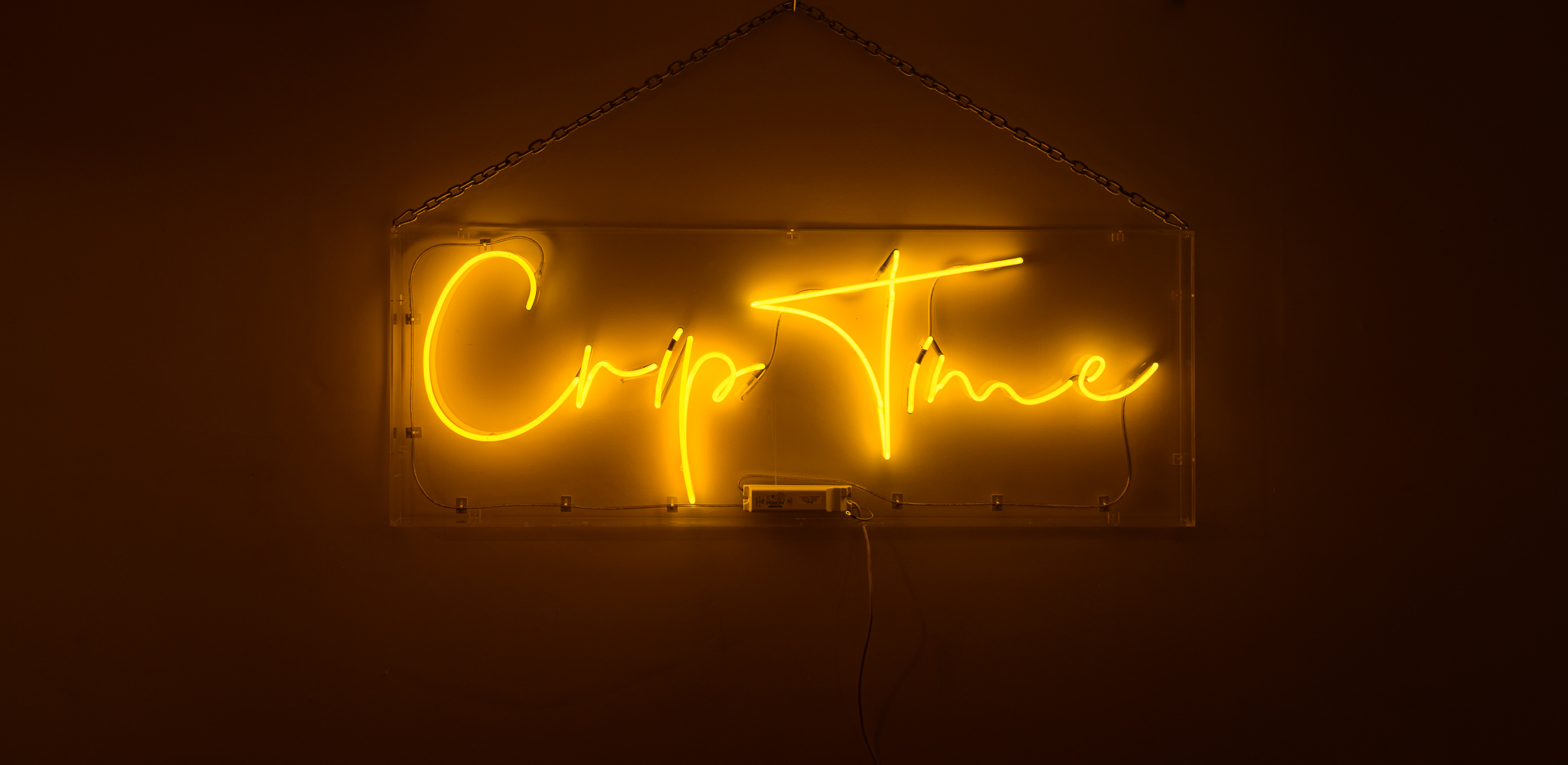 The wording reads on the artwork, 'Crip Time', - bright yellow neon lights in a stylised handwritten font. The neon words are framed inside a transparent perspex box.