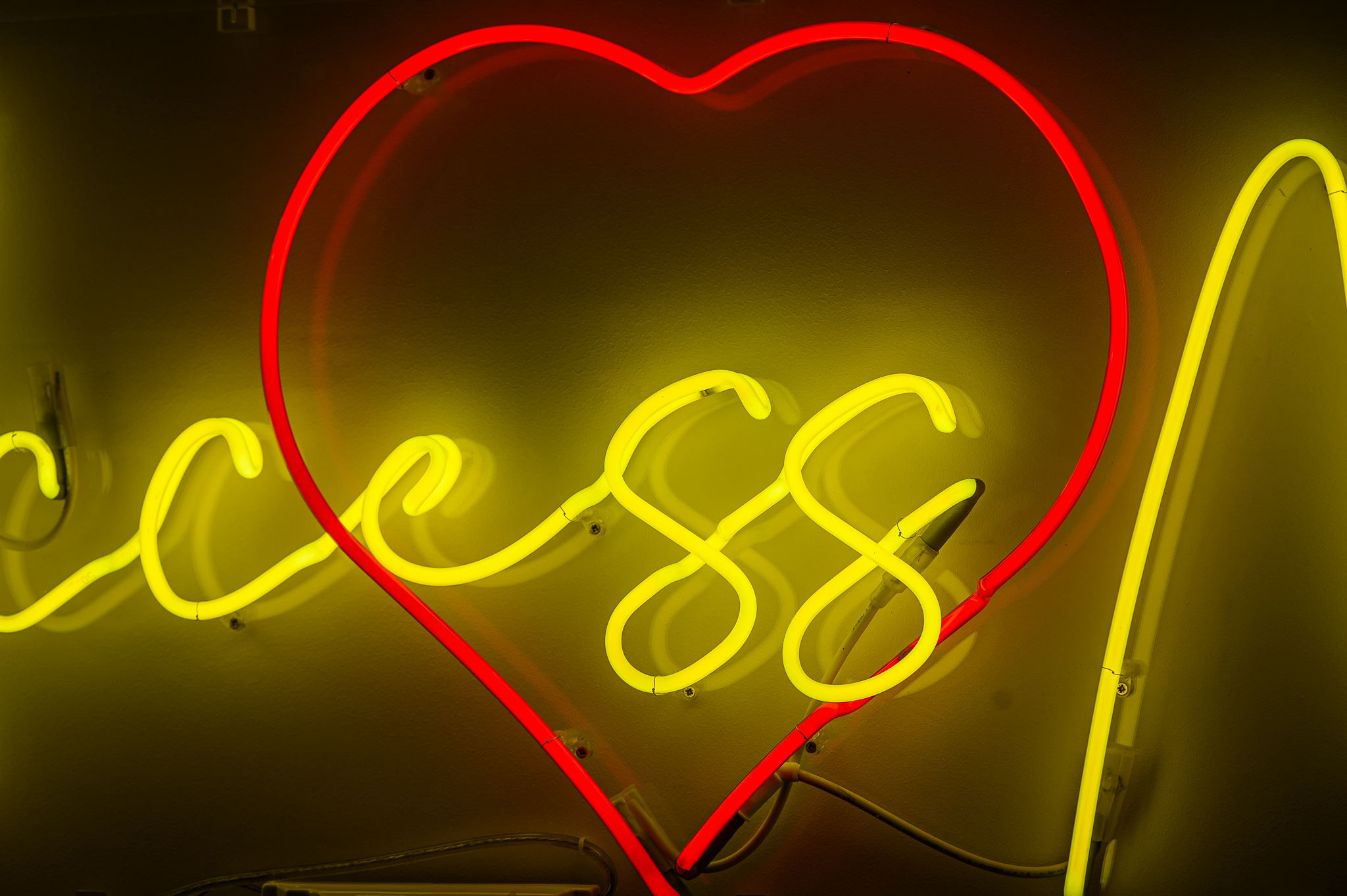 Close up photo of the neon love heart in red behind the wording, the neon lights are in a stylised handwritten font The neon words are framed inside a transparent Perspex box.