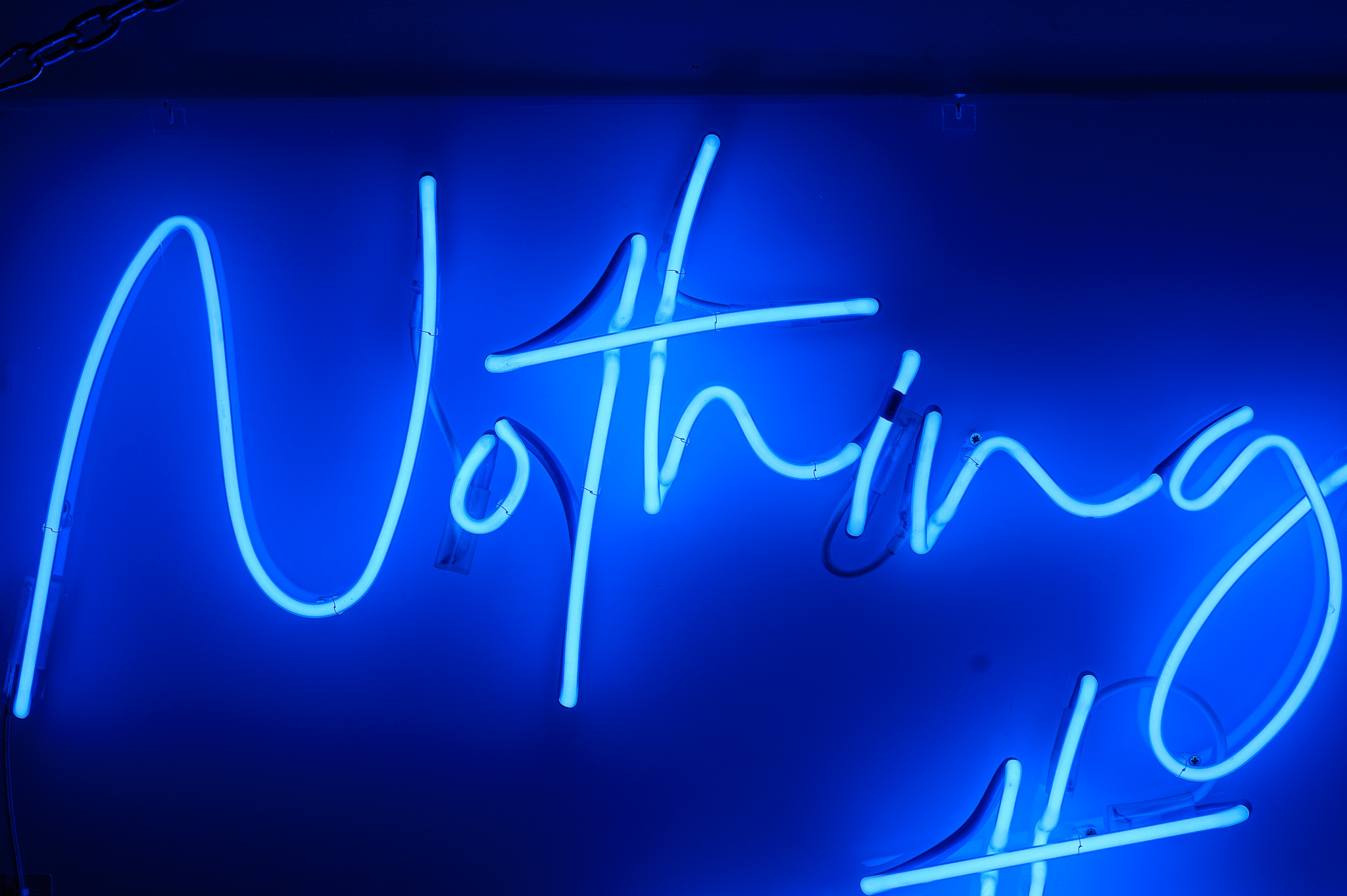 Close up photo of the word 'Nothing' in dark blue neon lights in a stylised handwritten font The neon words are framed inside a transparent Perspex box. 