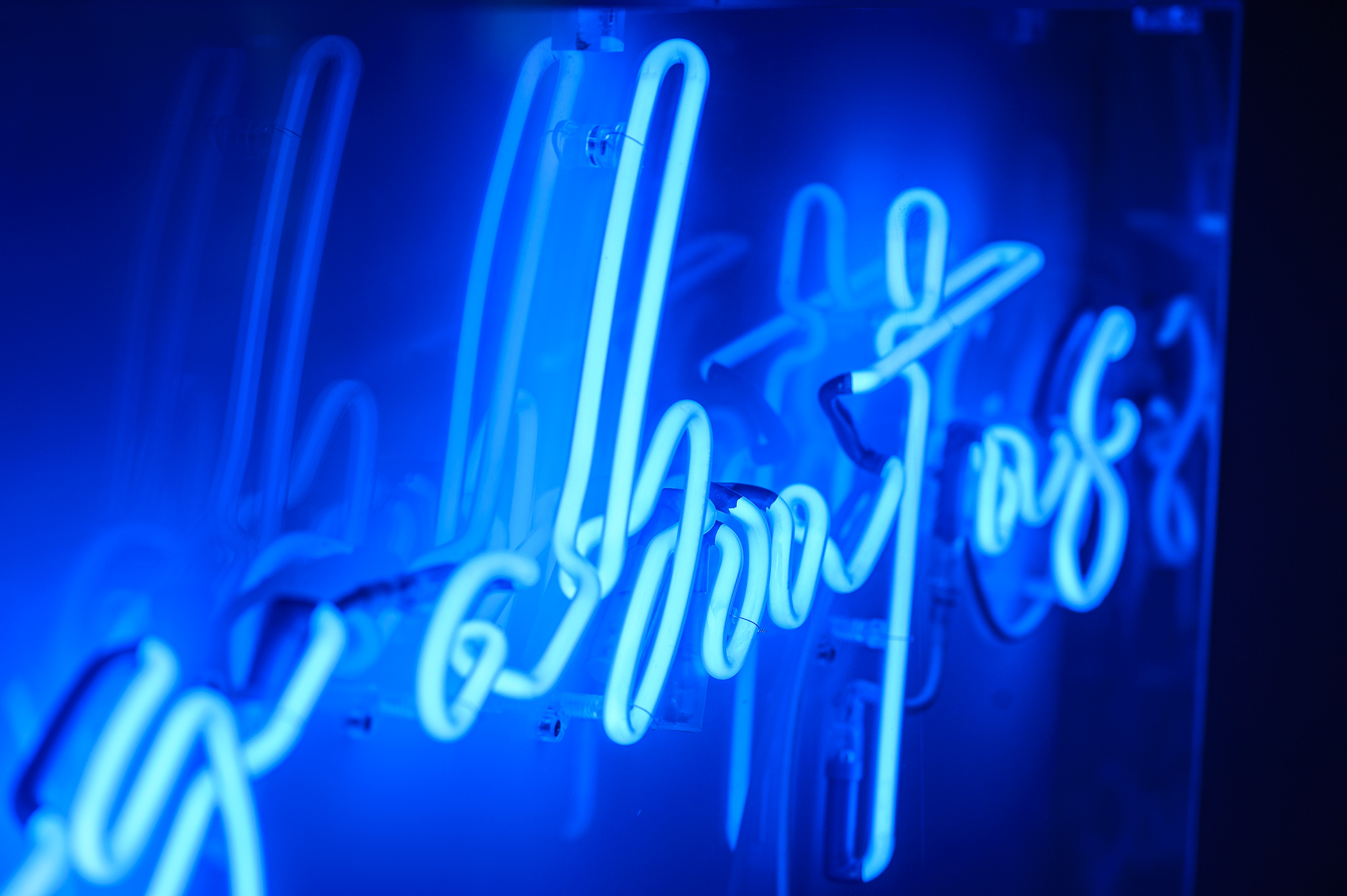 Close up photo of the word 'about' in dark blue neon lights in a stylised handwritten font The neon words are framed inside a transparent Perspex box. 