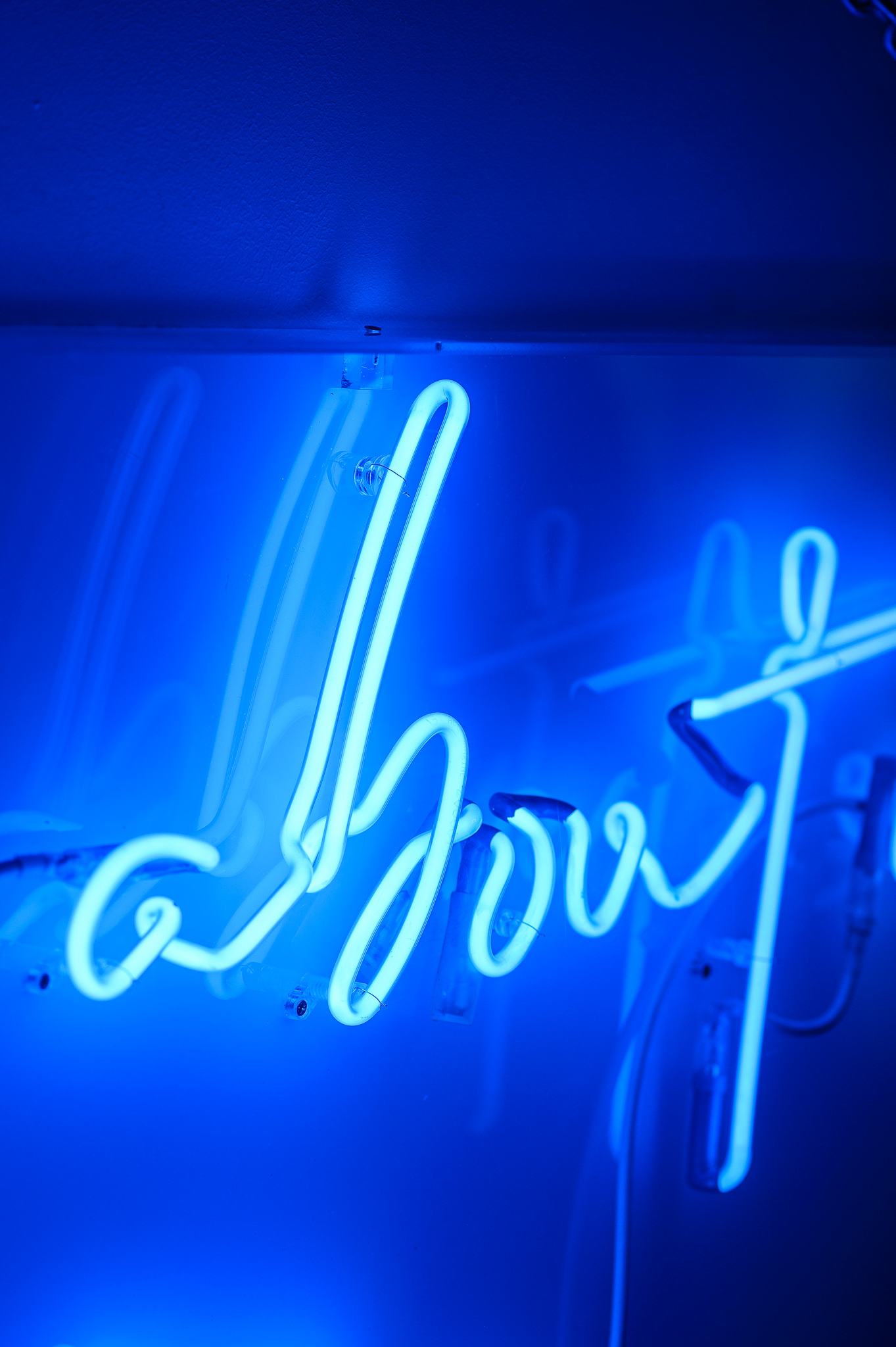 Close up photo of the word 'about' in dark blue neon lights in a stylised handwritten font The neon words are framed inside a transparent Perspex box. 