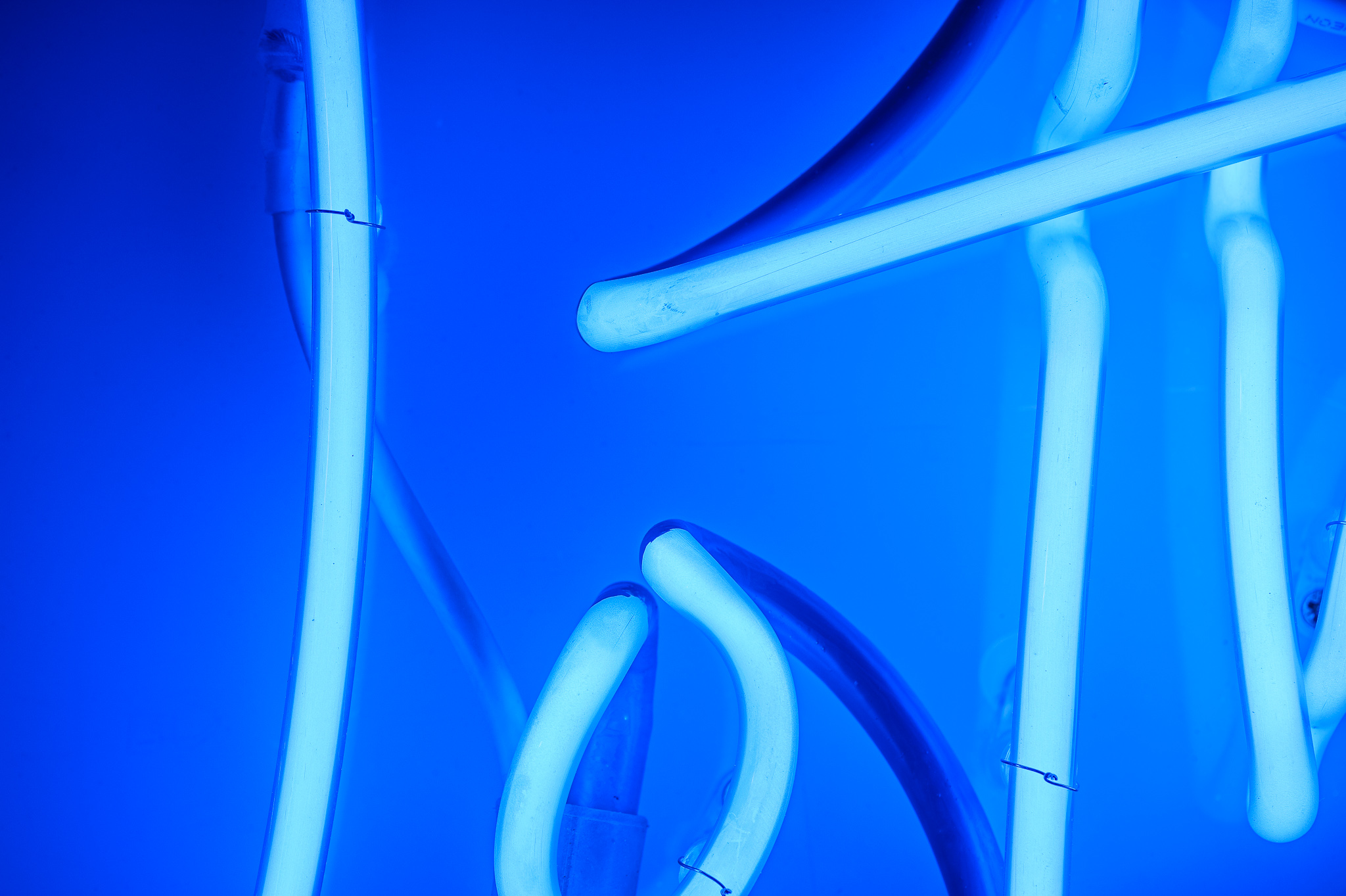 Close up photo of the artwork in dark blue neon lights in a stylised handwritten font The neon words are framed inside a transparent Perspex box. 